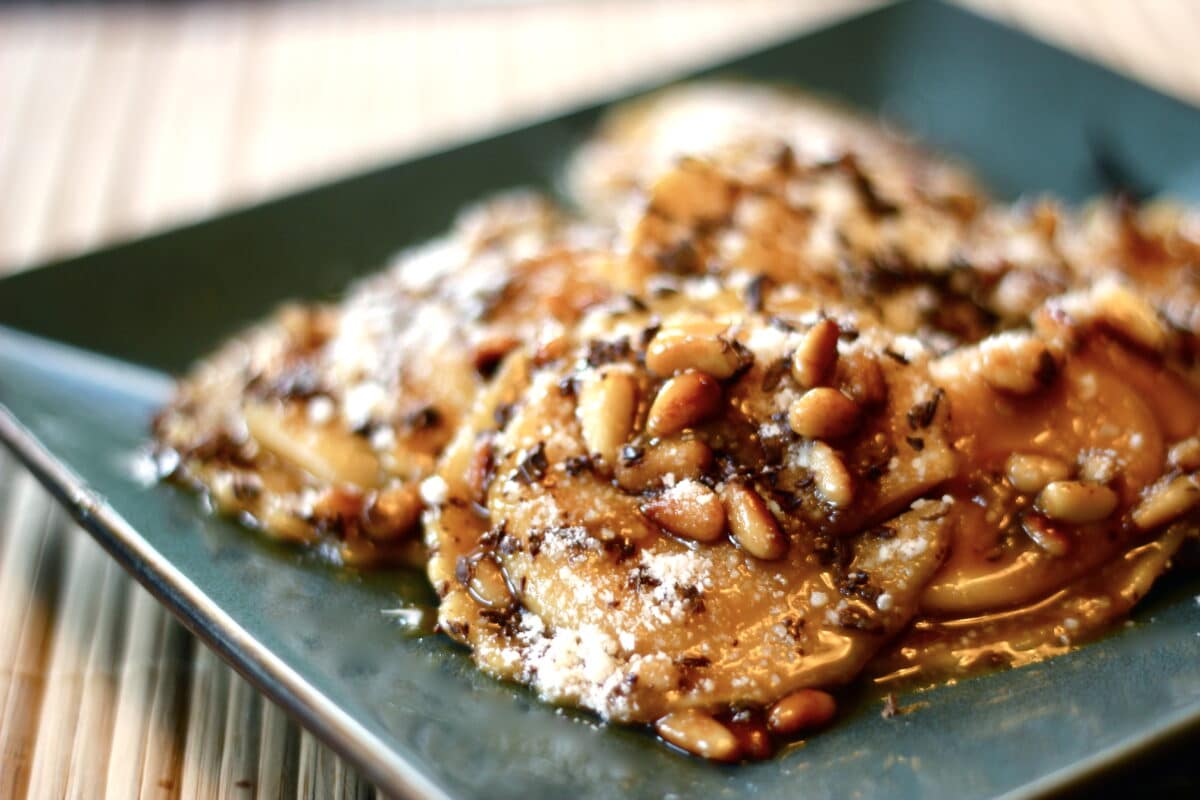 Plate of butternut squash ravioli with a buttery brown sugar sauce, parmesan cheese, toasted pine nuts, and chocolate shavings