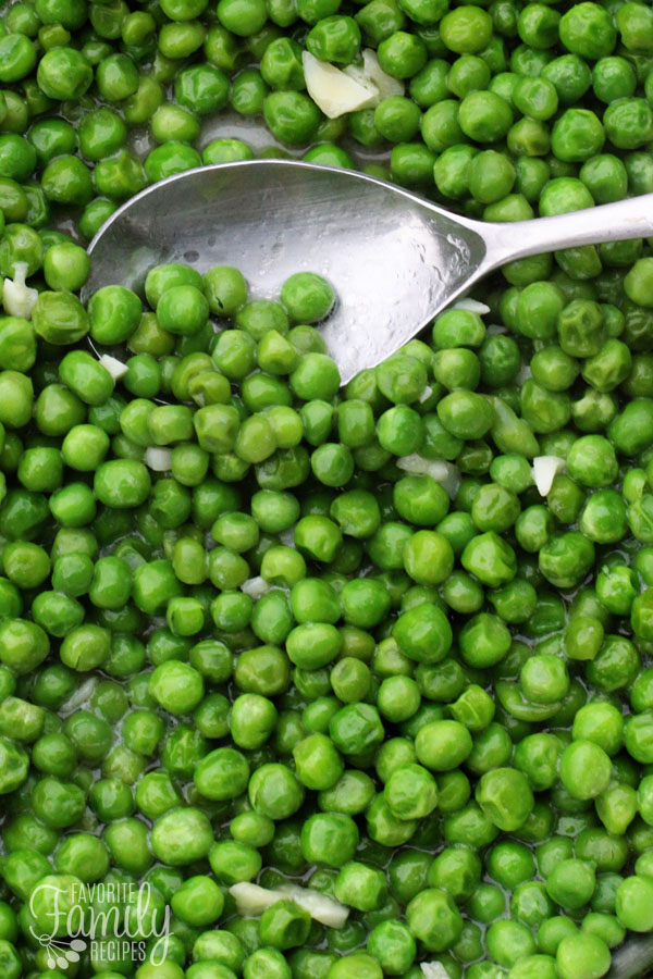 Seasoned and cooked frozen peas being scooped with a spoon