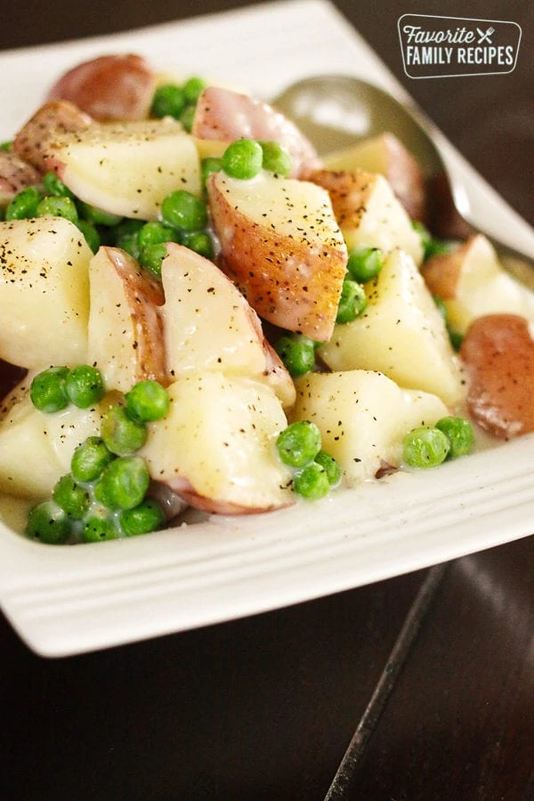 Pommes de terre crémeuses et petits pois sur une assiette blanche avec une cuillère sur le côté.