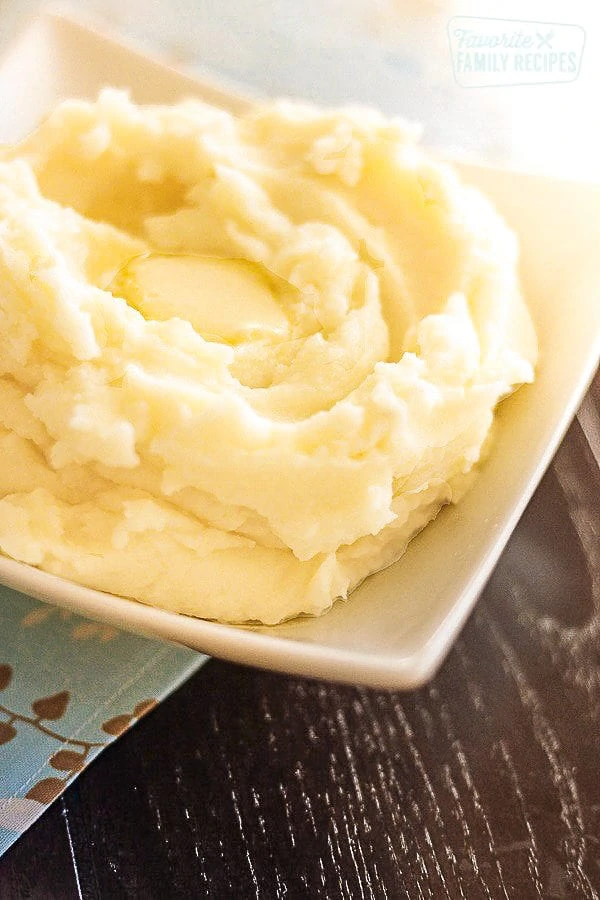 Un grand bol blanc rempli de purée de pommes de terre parfaite avec un carré de beurre fondant au centre