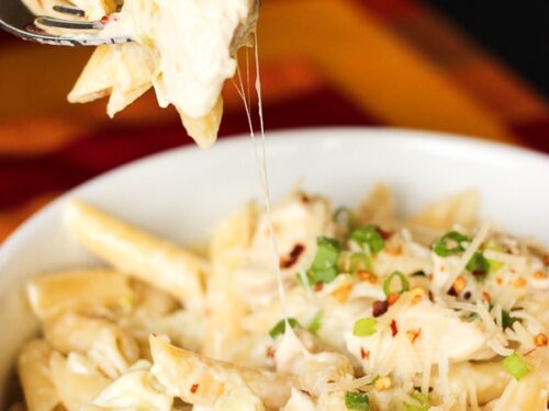 Pasta de pollo con alcachofas en un bol blanco con un tenedor.