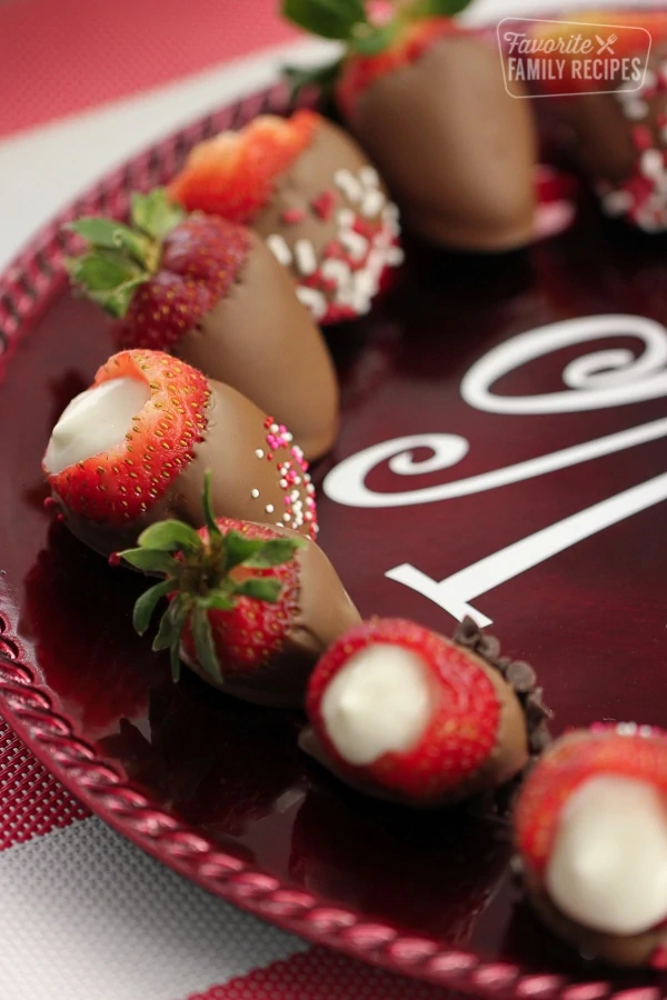 Fraises enrobées de chocolat fourrées au fromage sur une assiette marron.