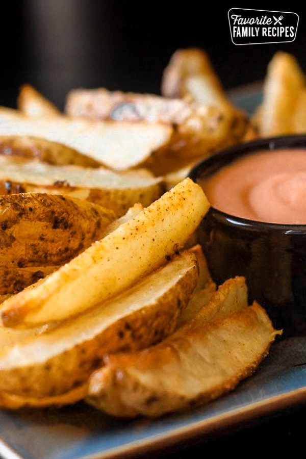 Morceaux de pommes de terre au four sur une assiette avec de la sauce friture dans un petit bol noir.