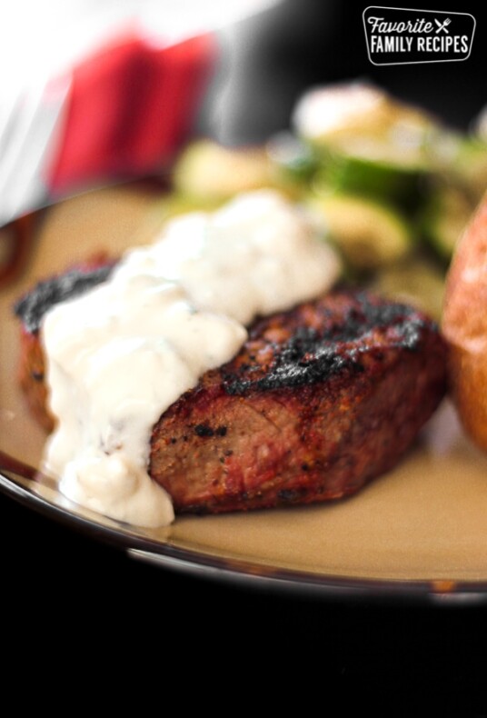 Filet Mignon topped with Melted Blue Cheese Sauce on a tan plate.