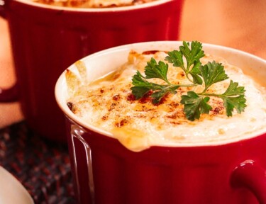 French Onion Soup in a red mug topped with a garnish.