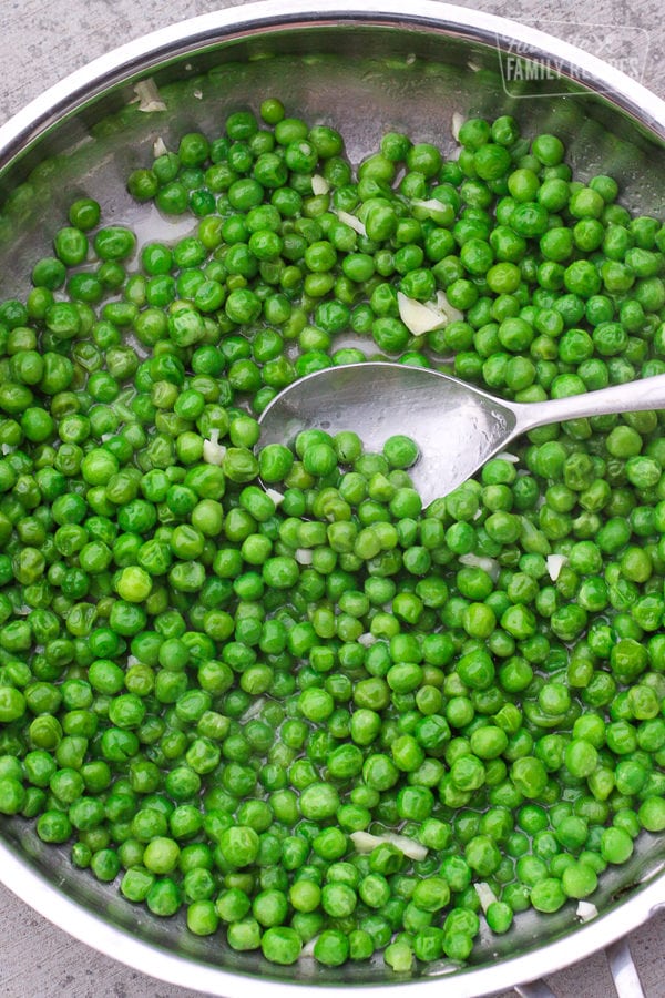 Cooked Frozen Peas in a skillet with a spoon scooping up some peas