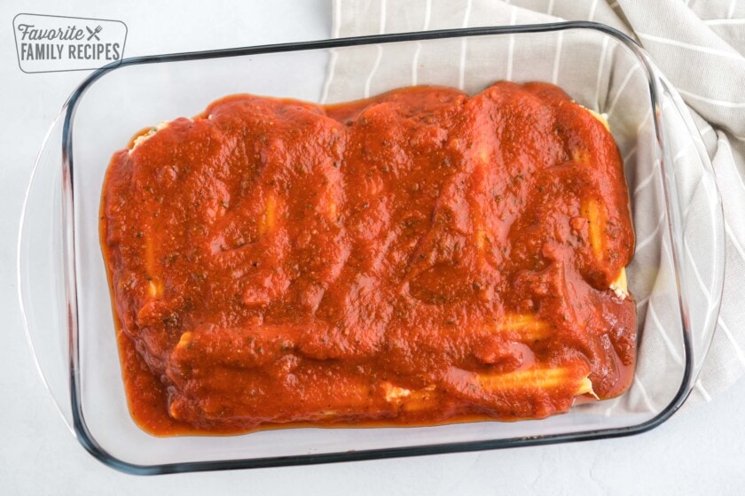 Layering manicotti with spaghetti sauce.