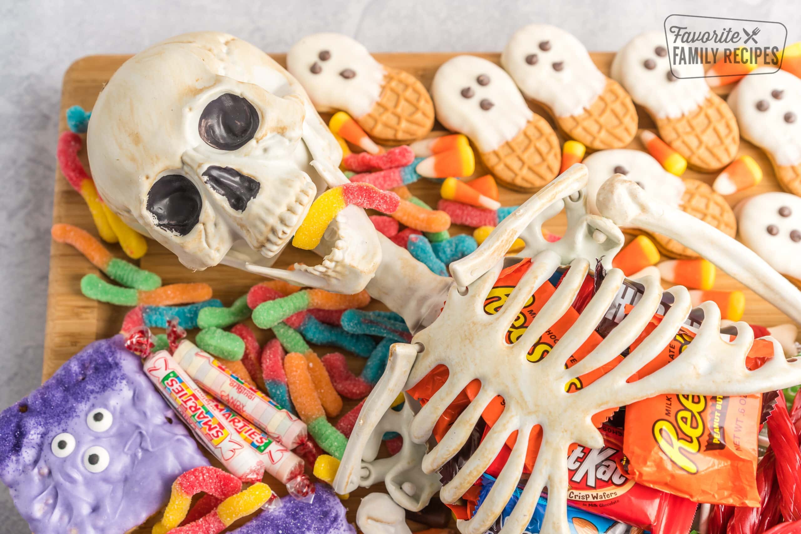 A skeleton charcuterie board with a skeleton in the middle surrounded by candies and chocolate snack candy bars