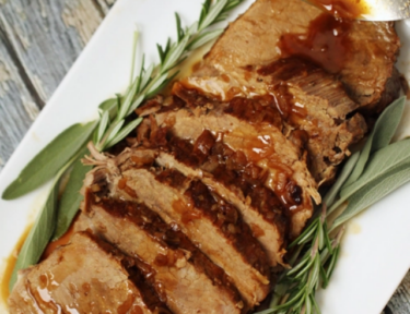 Slices of roast beef with gravy on top and rosemary garnish