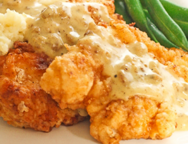 Chicken fried chicken on a plate with green beans and gravy poured over the top.