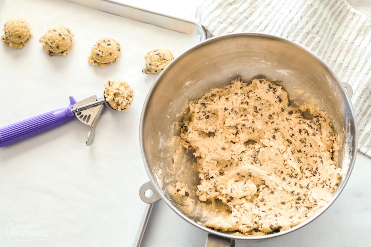 Cookie dough in a mixing bowl with scoops of cookie dough on a baking sheet with a cookie scoop.