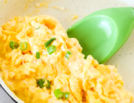 Close up of scrambled eggs in a pan with a green spatula underneath ready to lift the eggs from the pan.