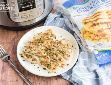 Sliced chicken on a plate with an instant pot and a bag of frozen chicken in the background