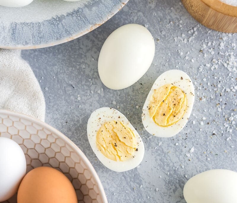 Peeled Hard Boiled Eggs on a plate with one egg cut in half and sprinkled with salt and pepper