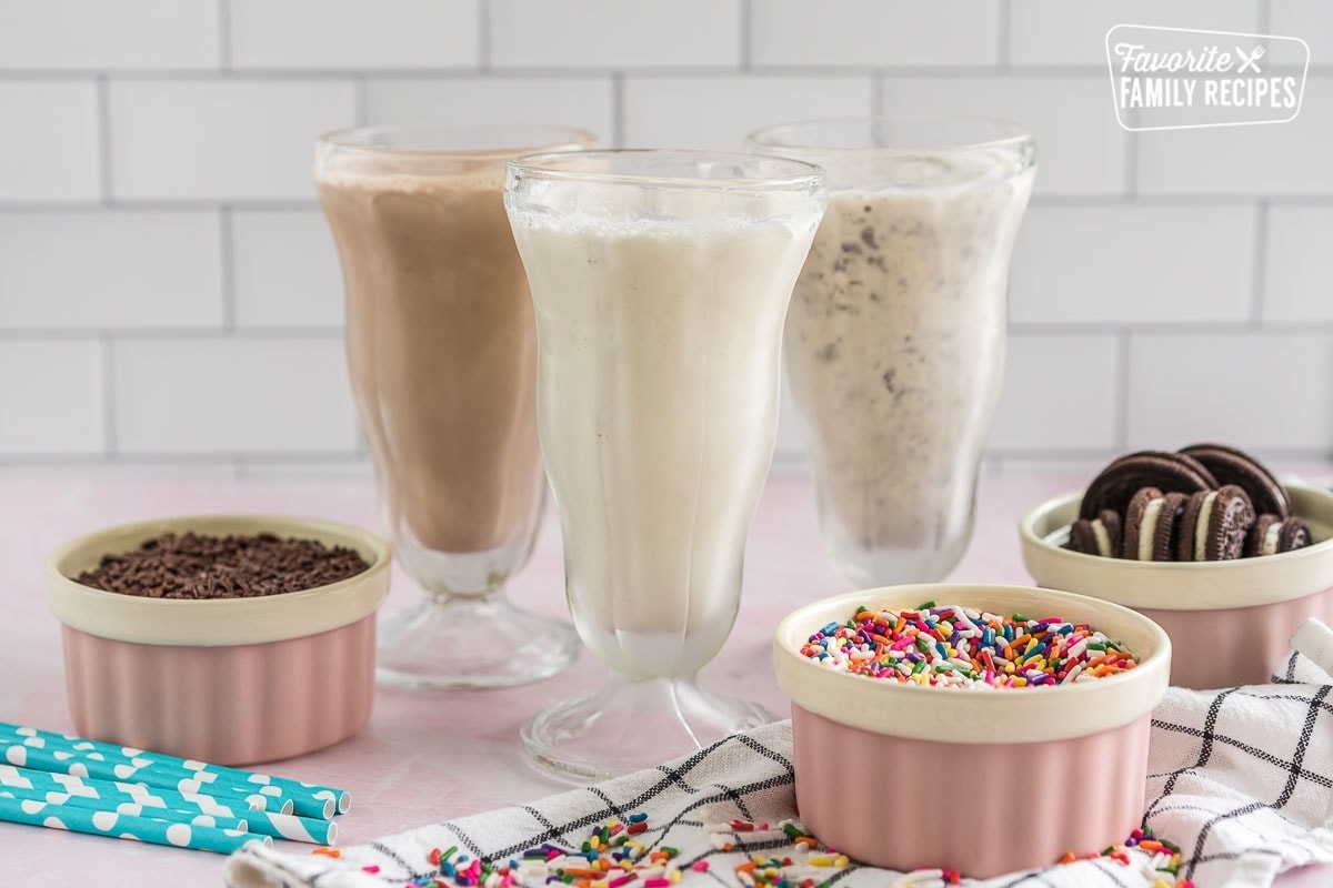 Three milkshakes in tall glasses, one vanilla, one chocolate, and one cookies and cream