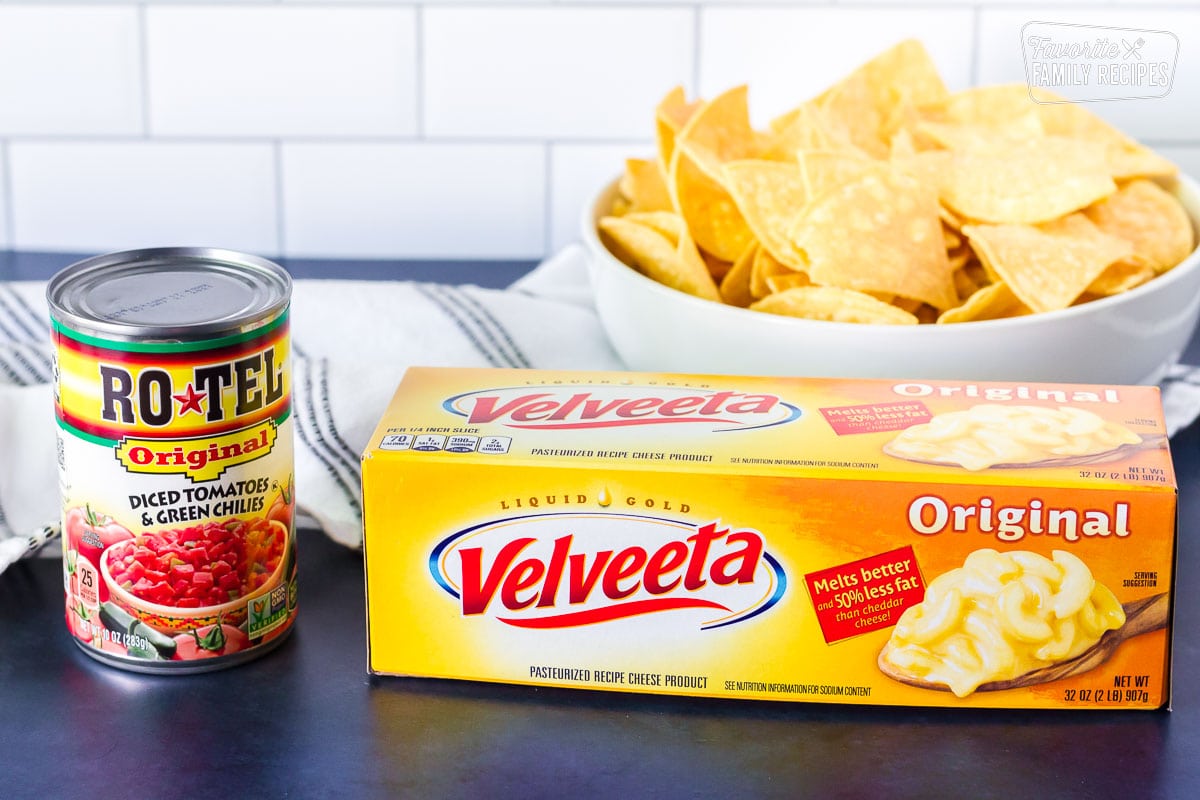 Can of Rotel Original diced tomatoes and green chilies, block of Velveeta cheese to make Nacho Cheese Dip. Large bowl of tortilla chips behind.