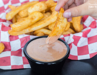 A basket of fries with one French fry being dipped into sauce.