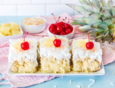 Three slices of Pina Colada Cake side by side. Garnished with cherries, pineapple and toasted coconut.