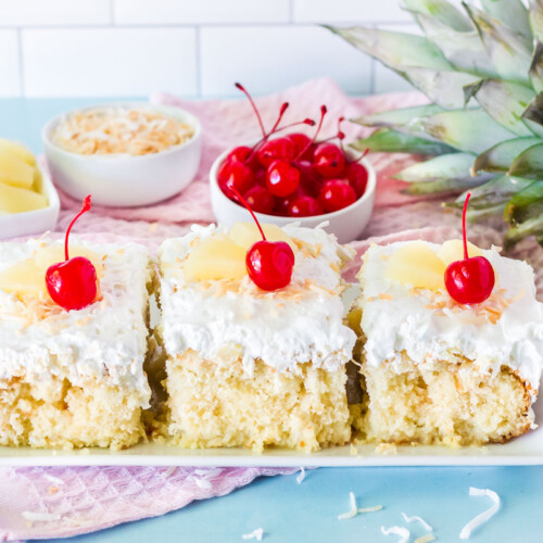 Three slices of Pina Colada Cake side by side. Garnished with cherries, pineapple and toasted coconut.