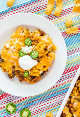 Frito Chili Pie on a plate with the serving tray to the side. Bag of Fritos with chips coming out on the side.