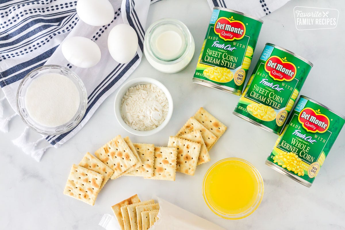 Ingredients for corn casserole display including canned corn, eggs, sugar, flour, milk, butter and saltine crackers