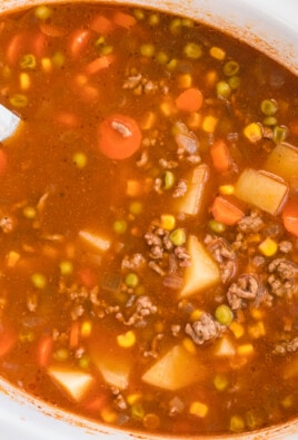 Homemade Crock Pot Vegetable Beef Soup, easy slow cooker soup with ground beef and vegetables, in a white slow cooker with a ladle.