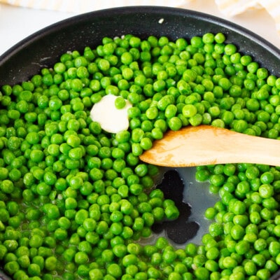 Wooden spoon stirring and cooking Frozen Peas.