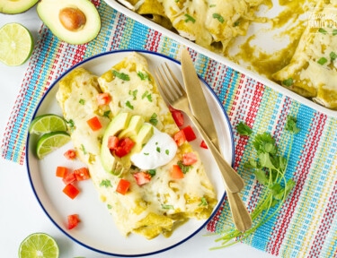 Plate with two Spinach Enchiladas topped with avocados, sour cream and tomatoes.