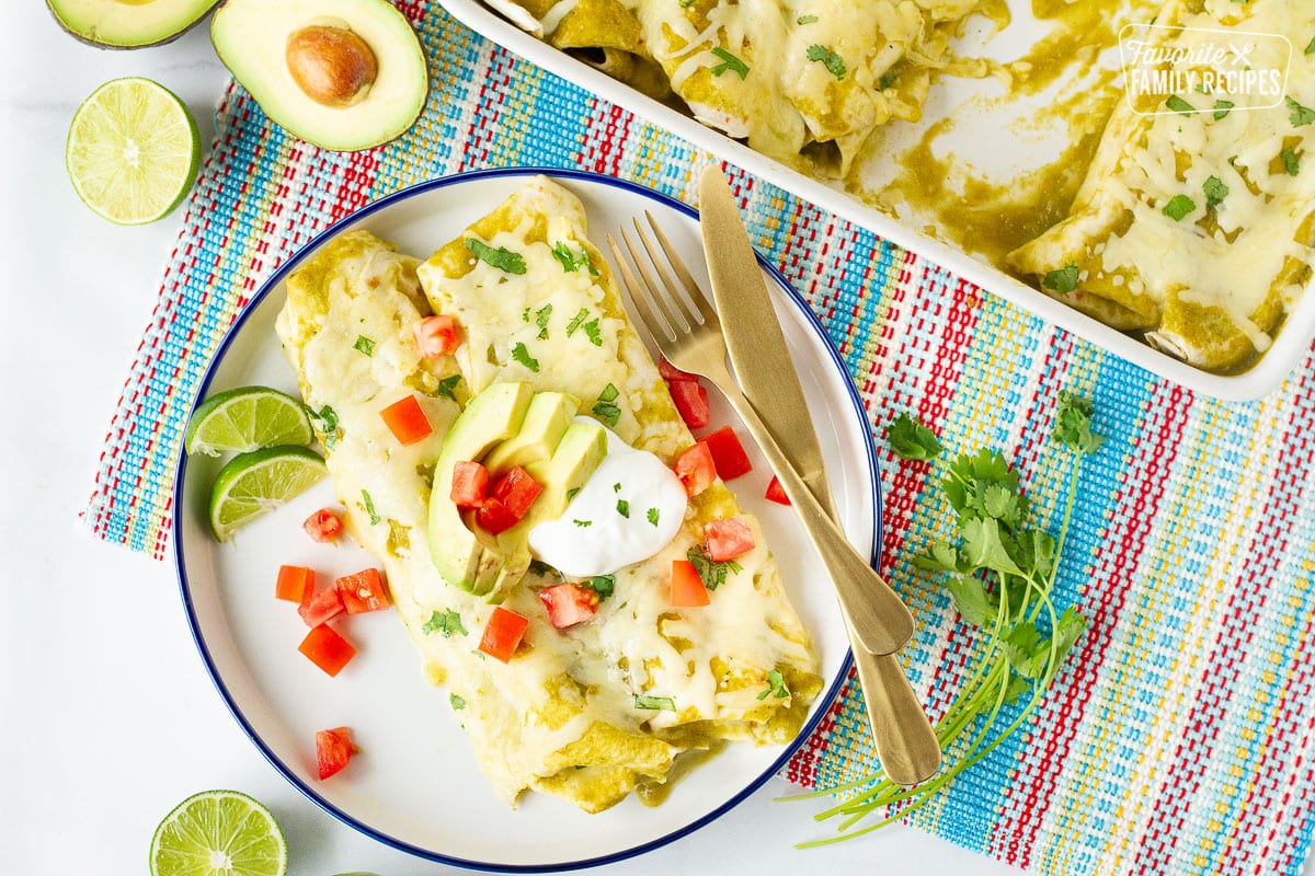 Plate with two Spinach Enchiladas topped with avocados, sour cream and tomatoes.