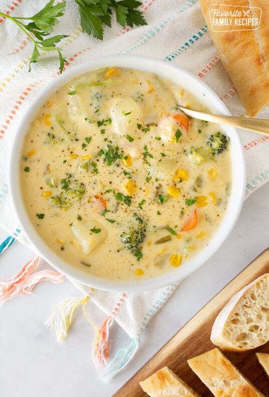 Creamy Vegetable Soup in a bowl with a spoon. Sliced French bread on the side.