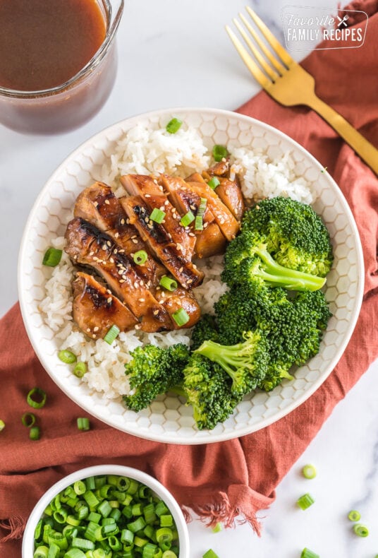 A bowl with rice, broccoli, and teriyaki chicken topped with sesame seeds and green onion