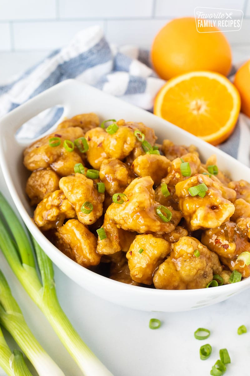 Bowl of homemade orange chicken coated in a zesty orange sauce and garnished with green onions.