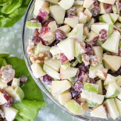 Waldorf Salad in a large glass bowl and a serving plate with the salad on a bed of lettuce next to it.