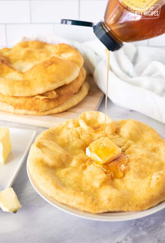 Pouring honey onto a piece of Fry Bread topped with butter.