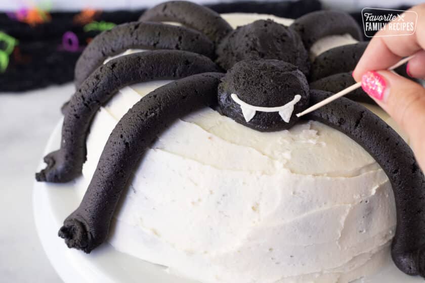 Hand holding a toothpick for fangs on a Spider Cake.