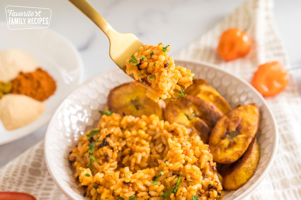 A forkful of jollof rice being taken out of a bowl.