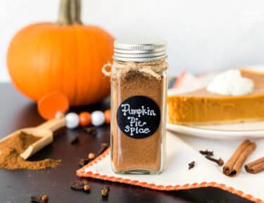 Pumpkin Pie Spice Substitute in a jar next to a pumpkin and slice of pumpkin pie.