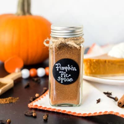 Pumpkin Pie Spice Substitute in a jar next to a pumpkin and slice of pumpkin pie.