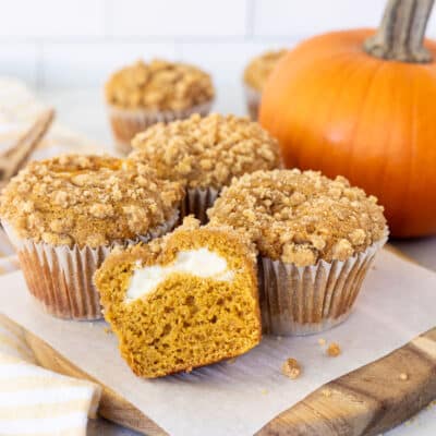 Pumpkin Cream Cheese Muffin sliced in half next to whole Pumpkin Cream Cheese Muffins.