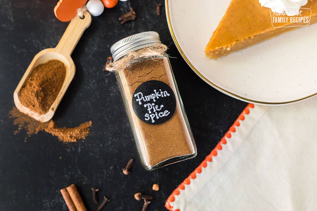 Jar of Pumpkin Pie Spice Substitute next to a scoop and slice of pumpkin pie.