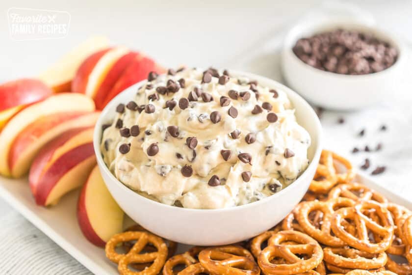 a bowl of chocolate chip cookie dough dip on a platter with pretzel twists and apple slices