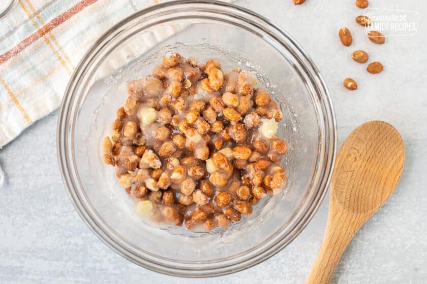 Mixing bowl with ingredients for Microwave Peanut Brittle combined. Wooden spoon on the side.