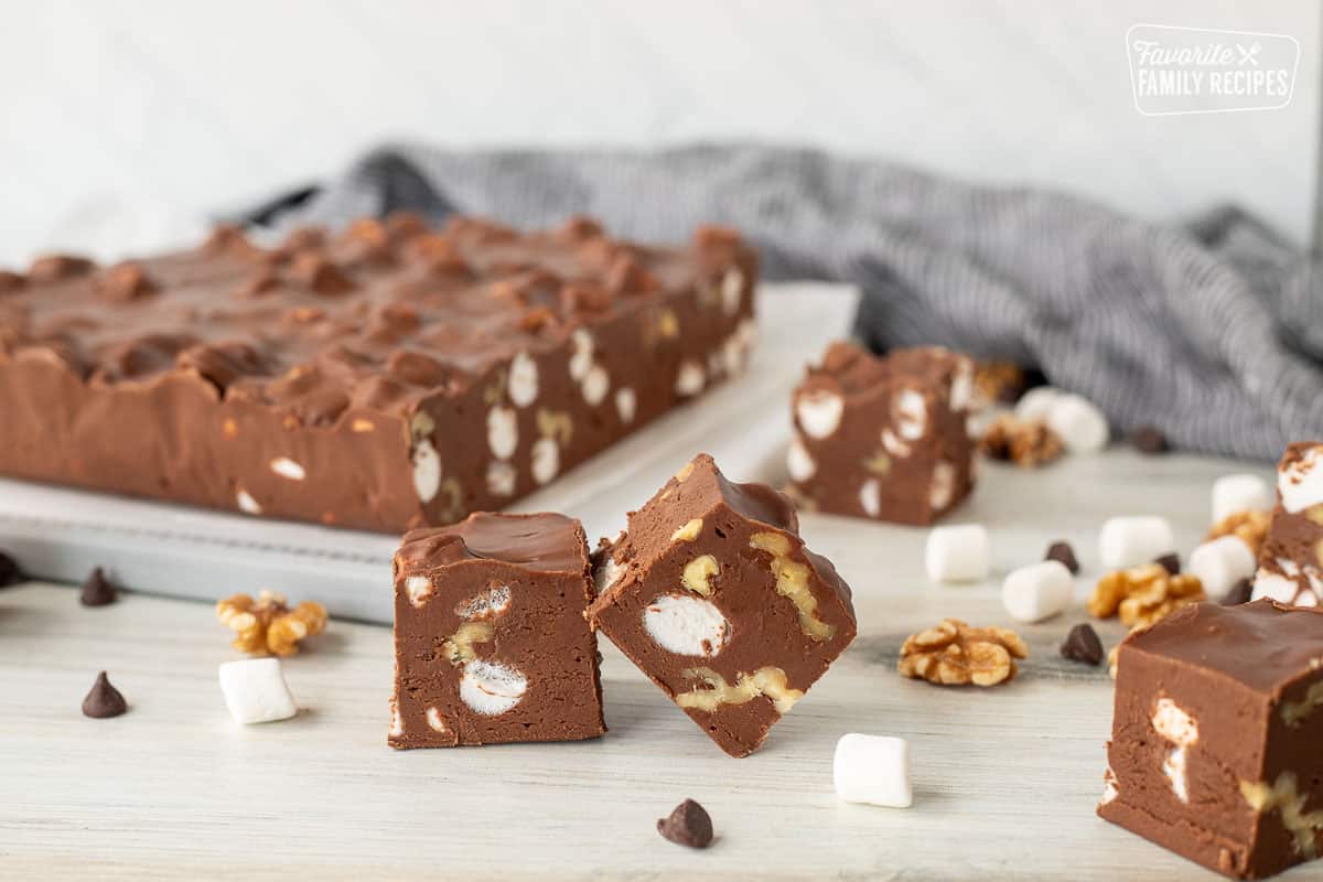 Two pieces of Marshmallow Rocky Road Fudge with slab of fudge in the background.