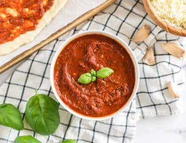 A bowl of homemade pizza sauce topped with basil leaves