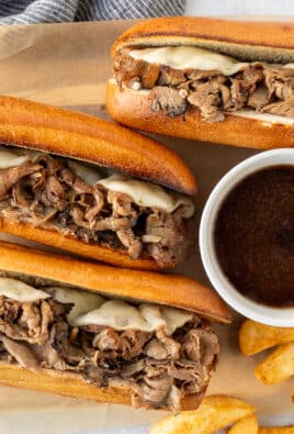 Three French Dip Sandwiches with toasted French bread, sliced roast beef and melted provolone cheese. Bowl of au jus and French fries on the side.