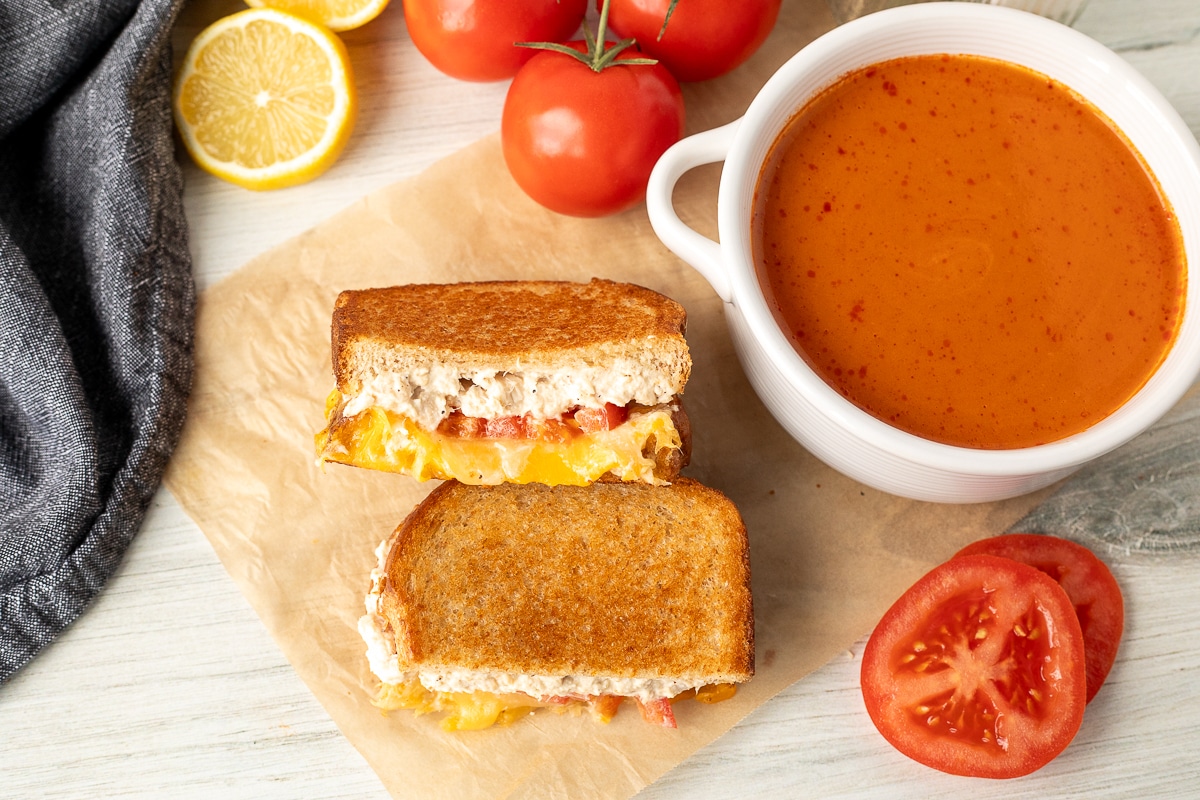 Two halves of a Tuna Melt Sandwich next to a bowl of tomato soup.