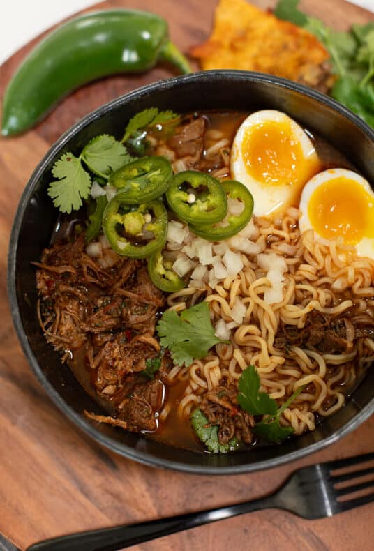 A bowl of birria ramen with cilantro, jalapeño, and soft boiled egg