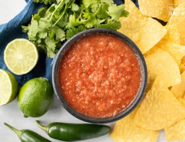 Bowl of Chili's copycat Salsa with tortilla chips, cilantro, limes and jalapeños.