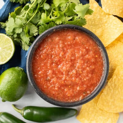 Bowl of Chili's copycat Salsa with tortilla chips, cilantro, limes and jalapeños.