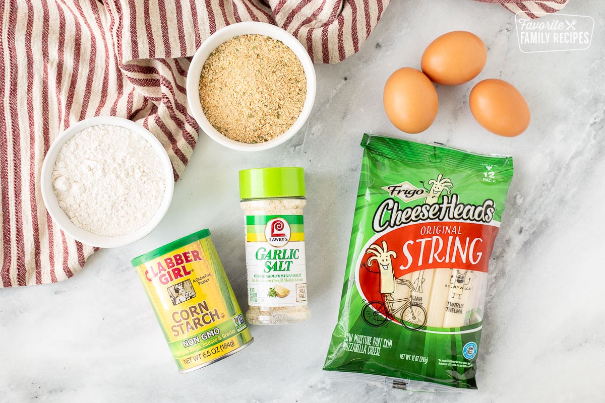 Ingredients to make homemade mozzarella sticks including string cheese, garlic salt, corn starch, flour, Italian bread crumbs and eggs.